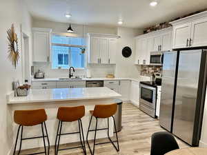 Kitchen with a peninsula, appliances with stainless steel finishes, white cabinets, and recessed lighting