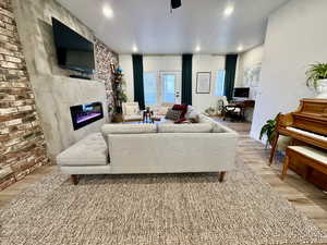 Living room featuring light wood finished floors, a glass covered fireplace, a ceiling fan, a desk, and recessed lighting