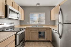 Kitchen with appliances with stainless steel finishes, light brown cabinetry, light countertops, light tile patterned floors, and a textured ceiling