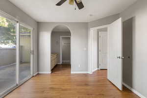 Unfurnished primary bedroom featuring arched walkways, light wood finished floors, access to exterior, connected bathroom, and a ceiling fan