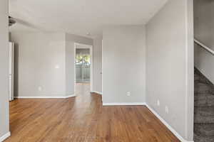 Empty room with stairs, wood-style floors, and a textured ceiling