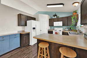 Kitchen featuring a breakfast bar area, white appliances, light countertops, dark brown cabinetry, and lofted ceiling