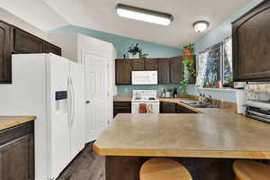 Kitchen featuring dark brown cabinets, white appliances, a breakfast bar area, and vaulted ceiling