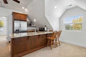 Kitchen with a textured ceiling, a kitchen breakfast bar, light stone countertops, light colored carpet, and healthy amount of natural light