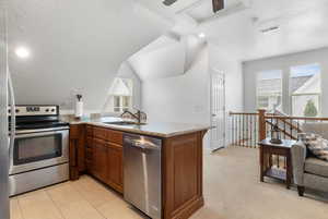 Kitchen with a peninsula, appliances with stainless steel finishes, a textured ceiling, light stone counters, and vaulted ceiling