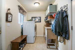 Washroom with light tile patterned floors, washer and clothes dryer, and cabinet space