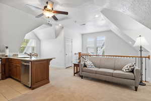 Kitchen with a peninsula, light carpet, light stone counters, dishwasher, and a textured ceiling