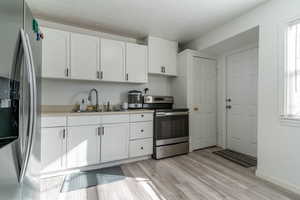 Kitchen featuring appliances with stainless steel finishes, white cabinets, light countertops, light wood finished floors, and plenty of natural light