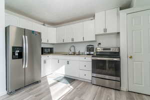 Kitchen with appliances with stainless steel finishes, white cabinetry, light countertops, and light wood-style floors