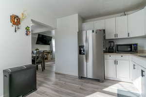 Kitchen with stainless steel appliances, white cabinetry, light wood-style floors, and light countertops