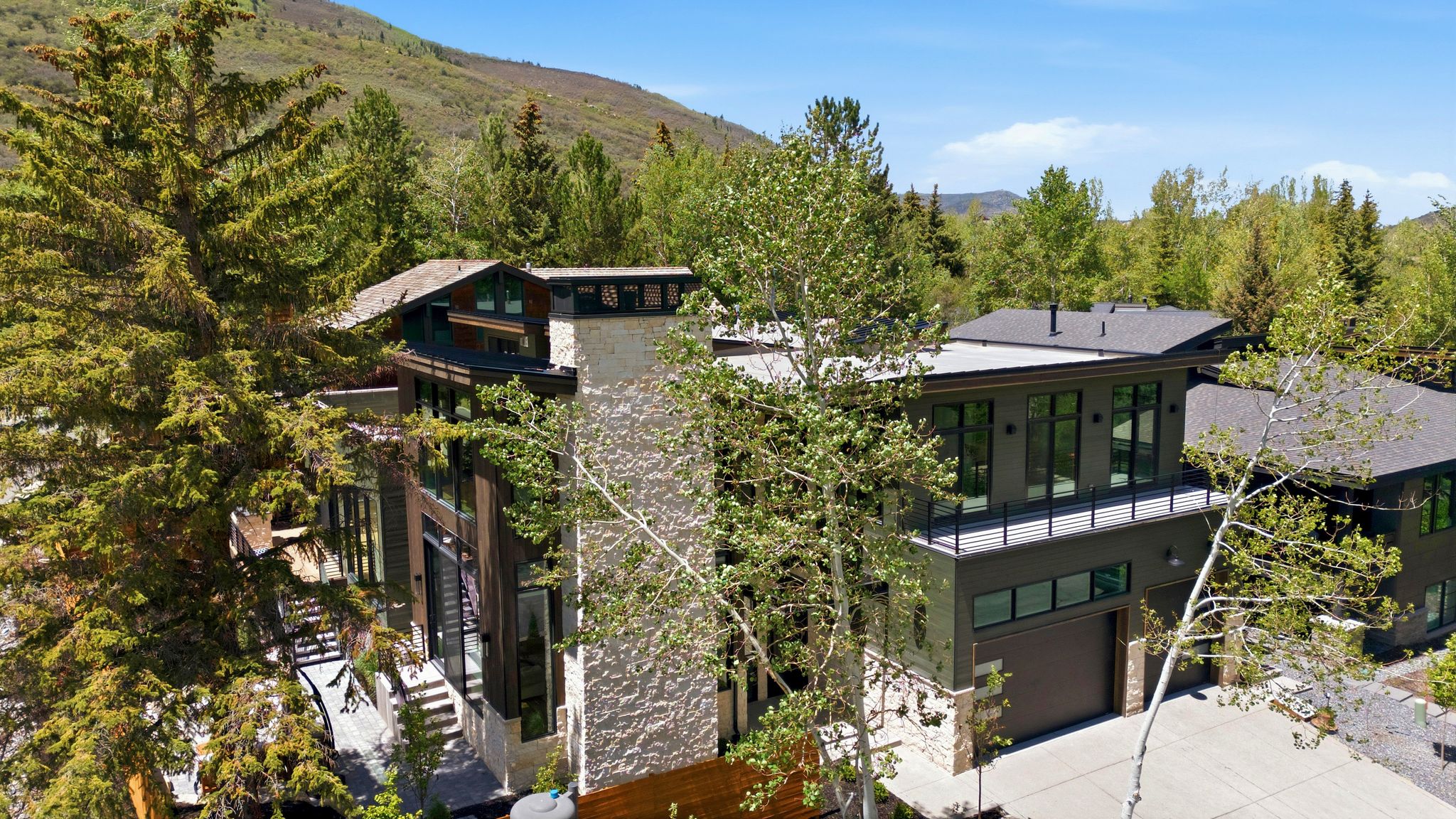 Contemporary multi-level residence featuring a stone-clad chimney, multiple outdoor balconies with black railings, and extensive window placements
