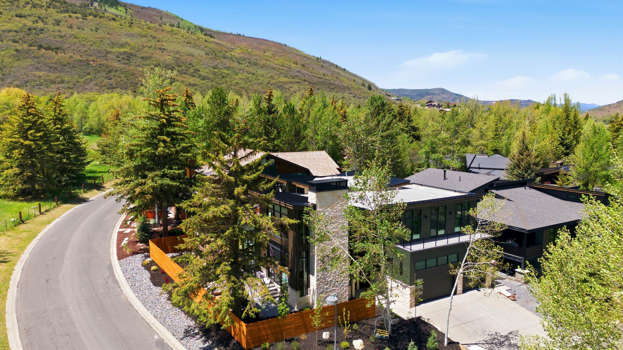 Modern architecture featuring a stone chimney, extensive dark-framed windows, multiple rooflines, and a paved driveway