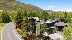 Modern architecture featuring a stone chimney, extensive dark-framed windows, multiple rooflines, and a paved driveway
