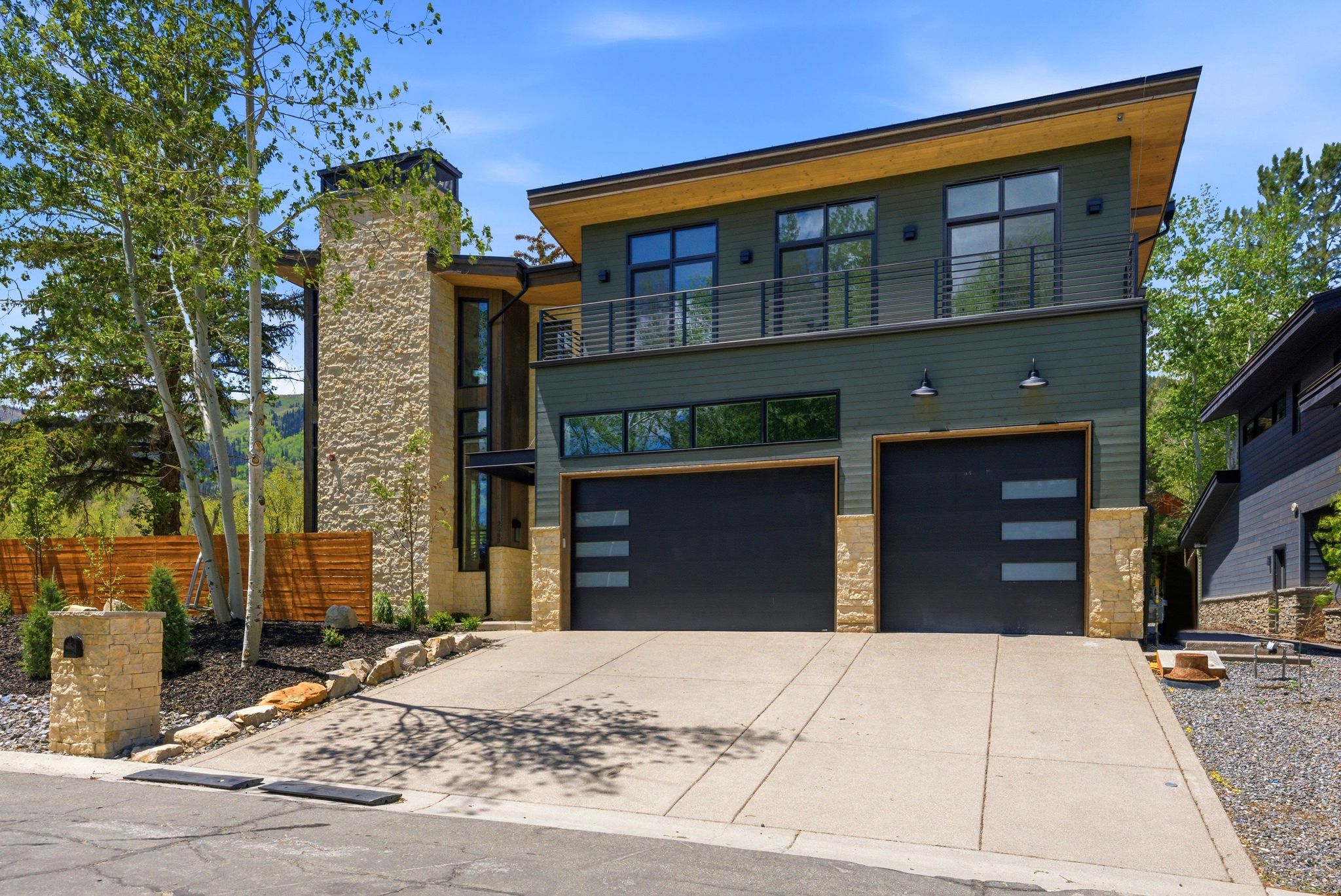 Contemporary exterior with a stone veneer facade, dark green horizontal siding, and a prominent two-car garage with modern doors