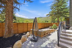 Paved patio area featuring paver flooring, a horizontal slat wood fence, mature landscaping with a large tree and decorative boulders, and exterior stairs with dark railings