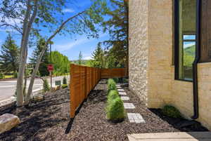 Stone veneer exterior with dark-framed windows, complemented by a wood privacy fence and a landscaped planting bed featuring stepping stones and manicured shrubbery