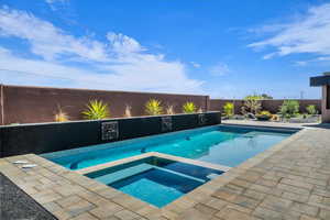 Combined pool / hot tub with a fenced backyard and a patio