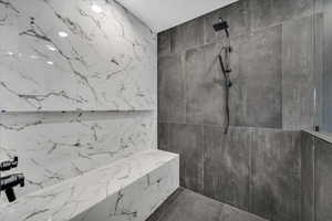 Full bathroom with tile walls, a marble finish shower, and stone wall