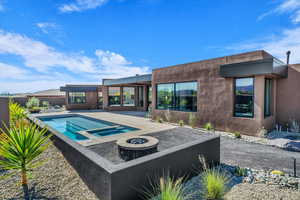 Back of house with a fire pit, stucco siding, a pool with connected hot tub, and a patio area