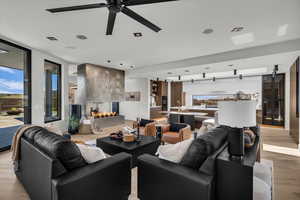 Living area with light wood-style floors, a ceiling fan, a multi sided fireplace, and expansive windows