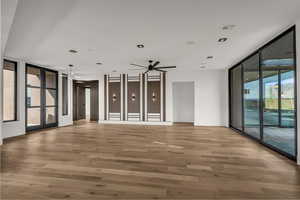 Empty room featuring expansive windows, a ceiling fan, french doors, and light wood finished floors