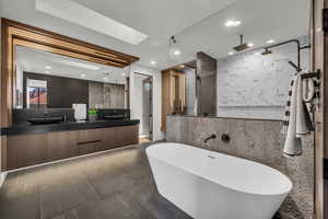 Bathroom with double vanity, a marble finish shower, a skylight, tile walls, and a freestanding bath