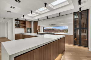 Kitchen with modern cabinets, a skylight, light stone counters, a large island, and brown cabinets