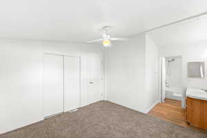 Unfurnished bedroom with light colored carpet, ceiling fan, a closet, ensuite bathroom, and light wood-style flooring