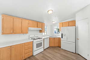 Kitchen with white appliances, light wood finished floors, light countertops, vaulted ceiling, and under cabinet range hood