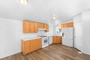 Kitchen with white appliances, light countertops, light wood-style flooring, lofted ceiling, and under cabinet range hood