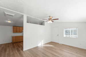 Empty room featuring light wood-style floors, a textured ceiling, lofted ceiling, and a ceiling fan