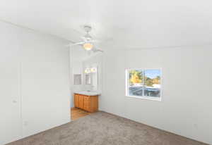 Unfurnished bedroom featuring light carpet, ensuite bath, ceiling fan, and lofted ceiling