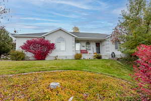 Ranch-style house with a porch, a front yard, stucco siding, and a shingled roof