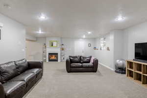 Carpeted living room featuring a glass covered fireplace, a textured ceiling, and recessed lighting