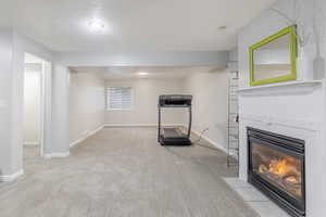 Exercise room featuring light carpet, a fireplace with flush hearth, and a textured ceiling