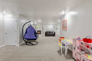 Recreation room featuring a warm lit fireplace, light carpet, and a textured ceiling
