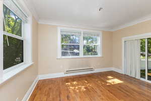 Spare room with wood finished floors, baseboard heating, and crown molding