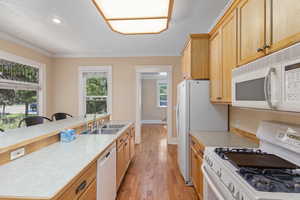 Kitchen with white appliances, light countertops, light wood-style floors, a kitchen island with sink, and a kitchen breakfast bar