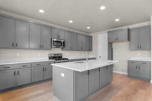 Kitchen featuring gray cabinets, light wood-style floors, recessed lighting, stainless steel appliances, and an island with sink