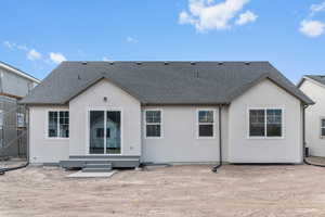 Back of house featuring roof with shingles and stucco siding