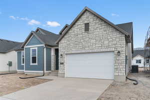 View of front of property featuring stone siding, driveway, roof with shingles, and an attached garage