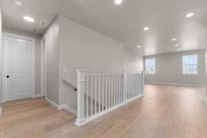 Hallway with an upstairs landing, recessed lighting, and light wood finished floors