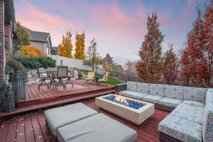 Deck at dusk with a fire pit, a fenced backyard, and outdoor dining area