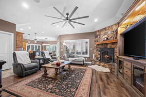 Living area featuring a stone fireplace, dark wood-style flooring, recessed lighting, a chandelier, and a ceiling fan