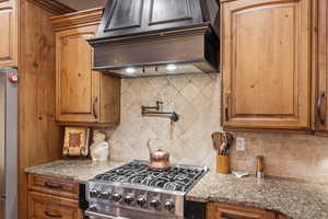 Kitchen with tasteful backsplash, custom exhaust hood, and light stone counters
