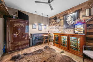 "Man Cave" Bar featuring wood finished floors, wood walls, a ceiling fan, and pendant lighting