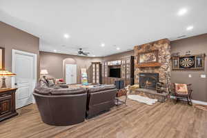 Living room with arched walkways, recessed lighting, wood finished floors, a fireplace, and a ceiling fan