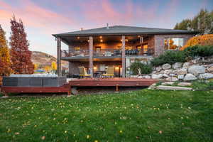 Back of house with brick siding, a wooden deck, a yard, a shingled roof, and a balcony