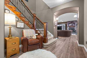 Living area with arched walkways, stairs, a stone fireplace, and wood finished floors