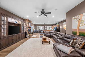 Living room featuring light wood-type flooring, arched walkways, a stone fireplace, recessed lighting, and a ceiling fan